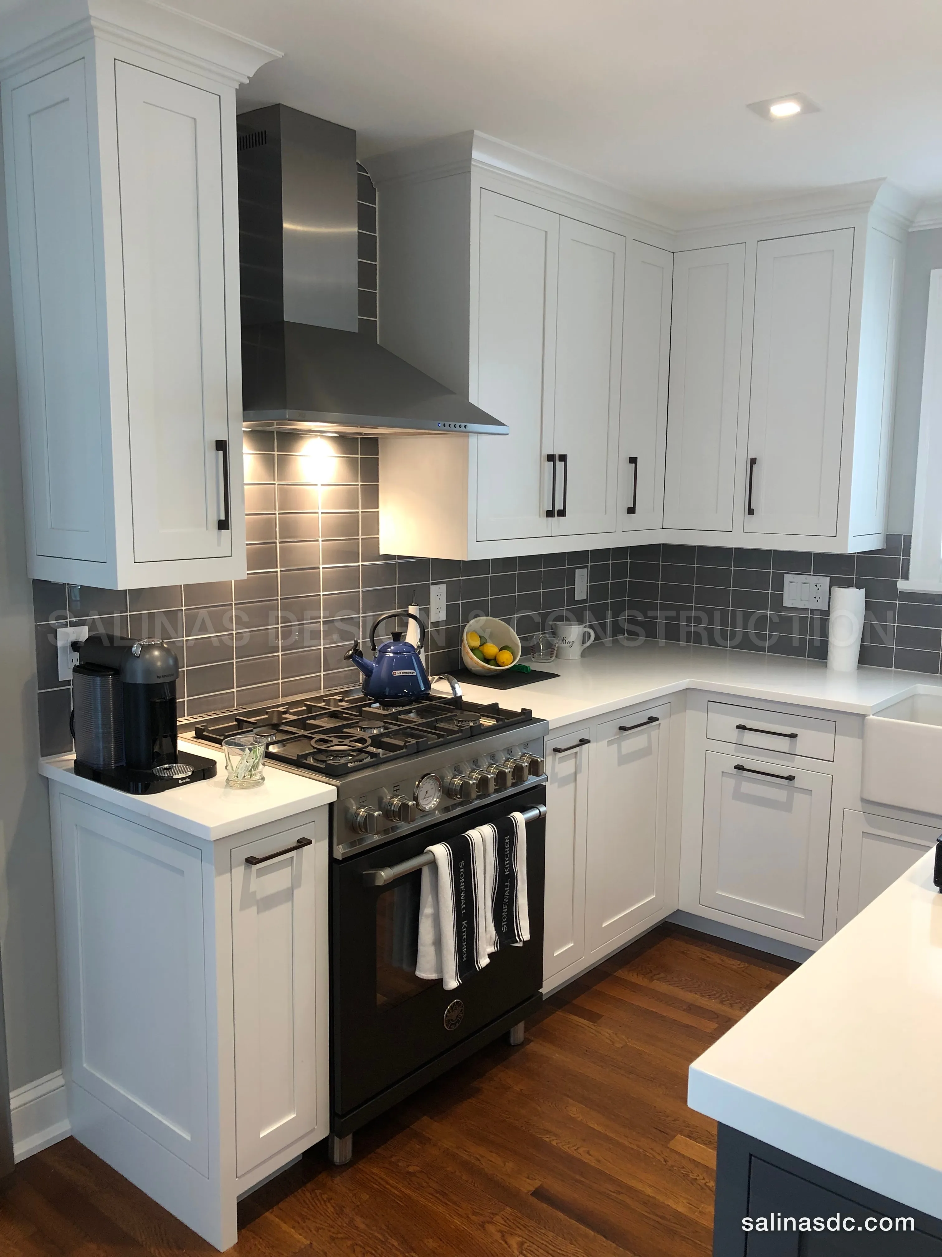 The same corner after the remodel: white shaker cabinets to the ceiling, a stainless hood, charcoal tile and white quartz, built and installed by Salinas Design and Construction